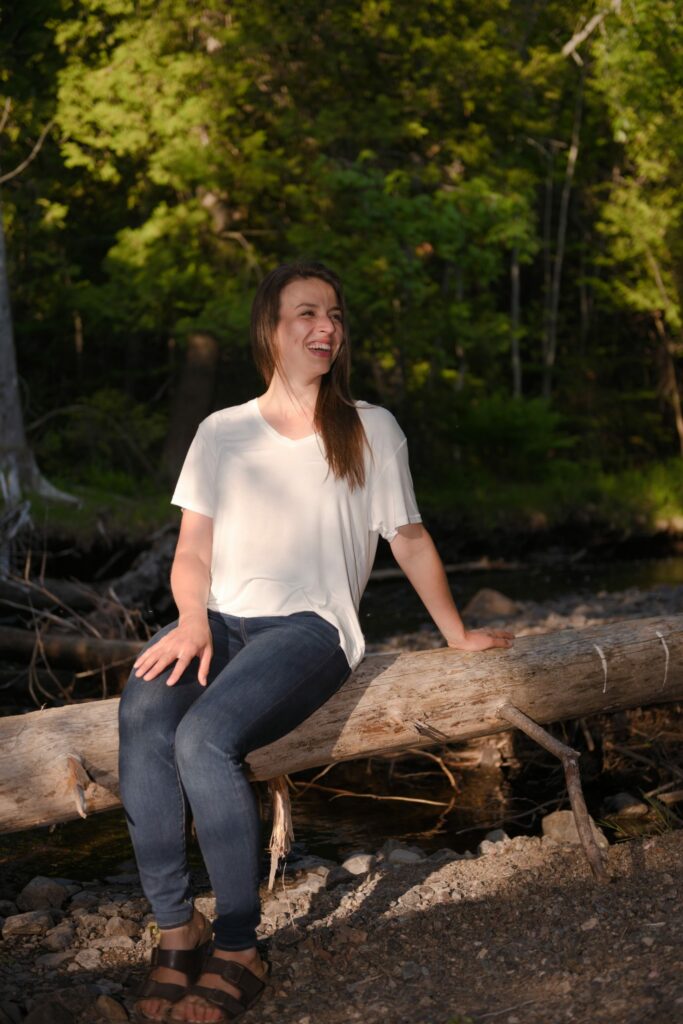 Ana McRae, life and business coach in the woods sitting on tree stump