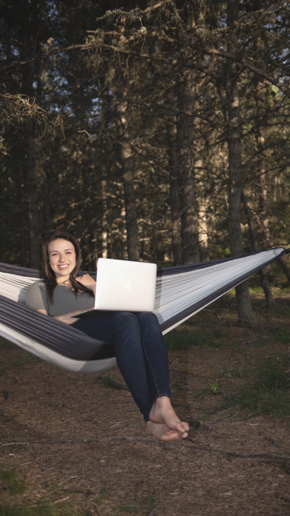 Ana McRae, Life and Business Coach sitting on hammock in forest using laptop