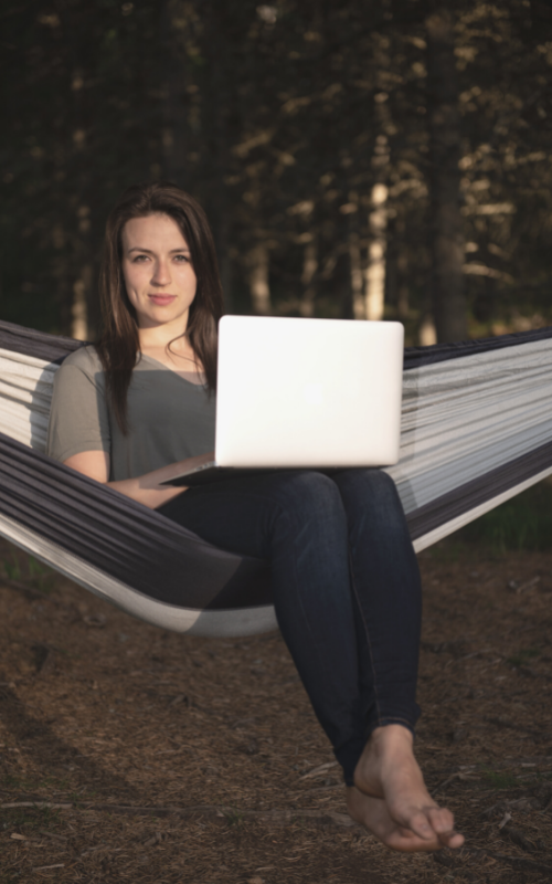 Ana McRae business success coach sitting on hammock working on laptop